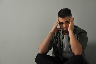 Photo of Sad man sitting near light grey wall. Space for text