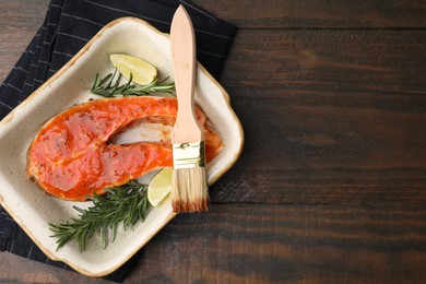 Photo of Fresh marinade, fish, rosemary, lime and brush on wooden table, top view. Space for text