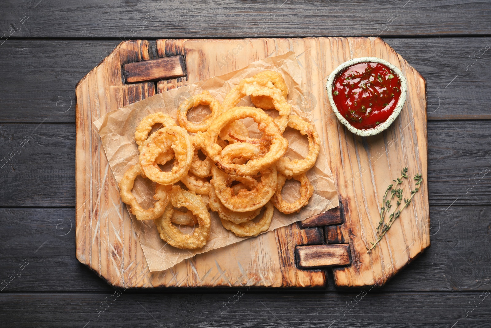 Photo of Homemade crunchy fried onion rings and sauce on wooden background, top view