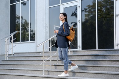 Photo of Beautiful young woman with stylish backpack and laptop near building outdoors