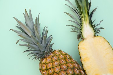 Photo of Whole and cut ripe pineapples on light green background, flat lay