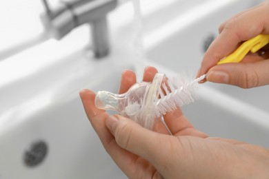 Photo of Woman washing baby bottle nipple indoors, closeup