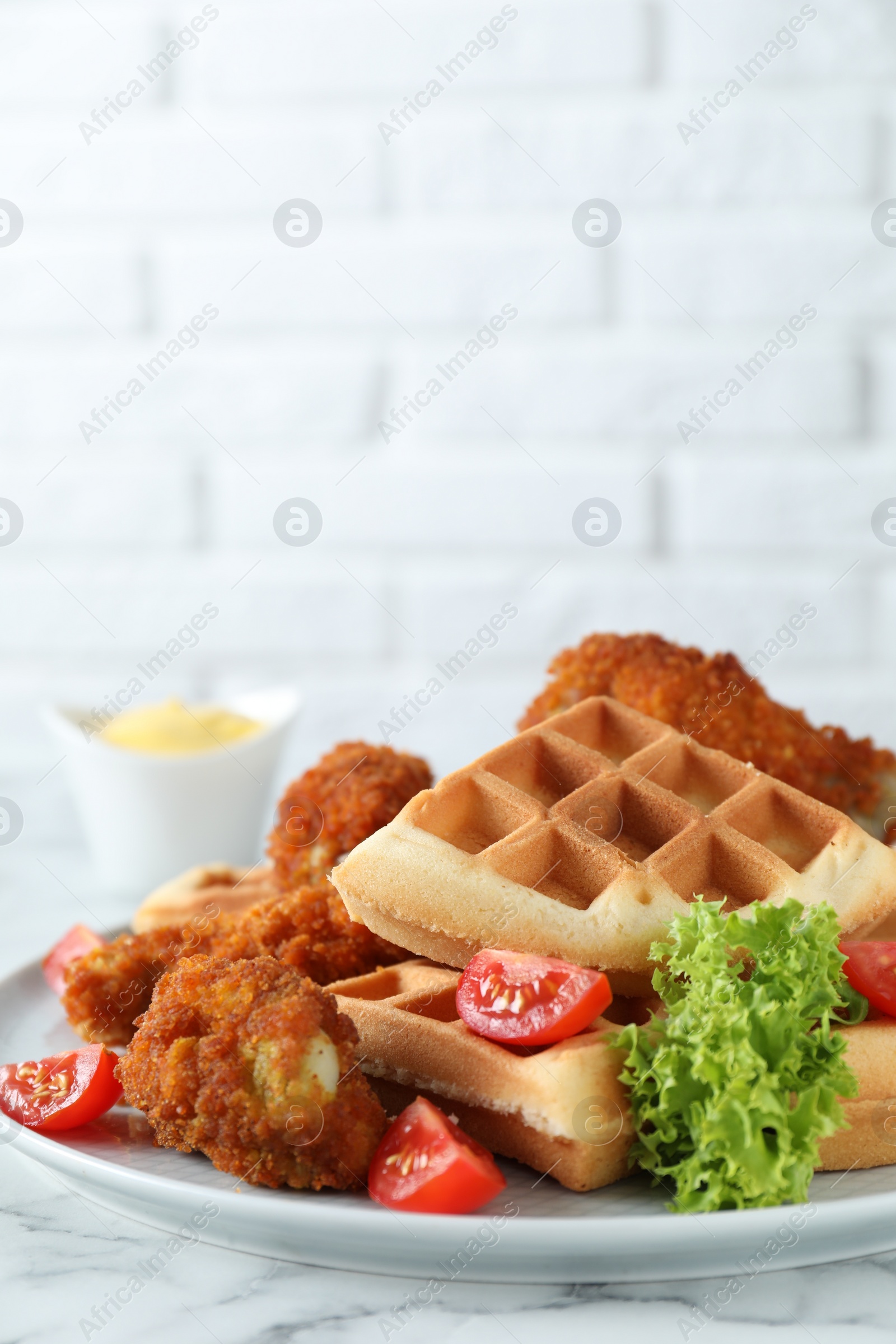 Photo of Tasty Belgian waffles served with fried chicken, tomatoes and lettuce on white marble table, closeup