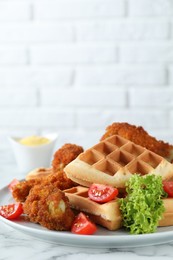 Tasty Belgian waffles served with fried chicken, tomatoes and lettuce on white marble table, closeup
