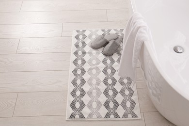 Photo of Soft bath mat and slippers on floor in bathroom