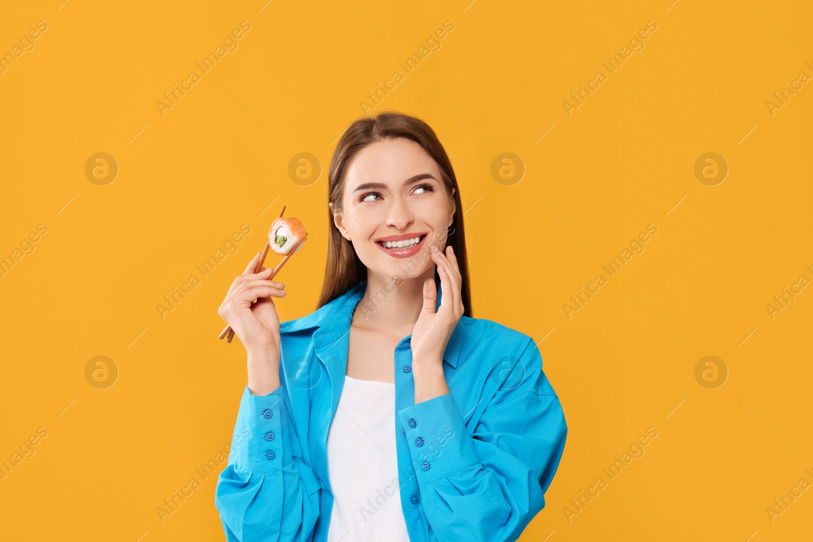 Photo of Happy beautiful young woman holding sushi roll with chopsticks on orange background
