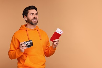 Smiling man with passport, camera and tickets on beige background. Space for text