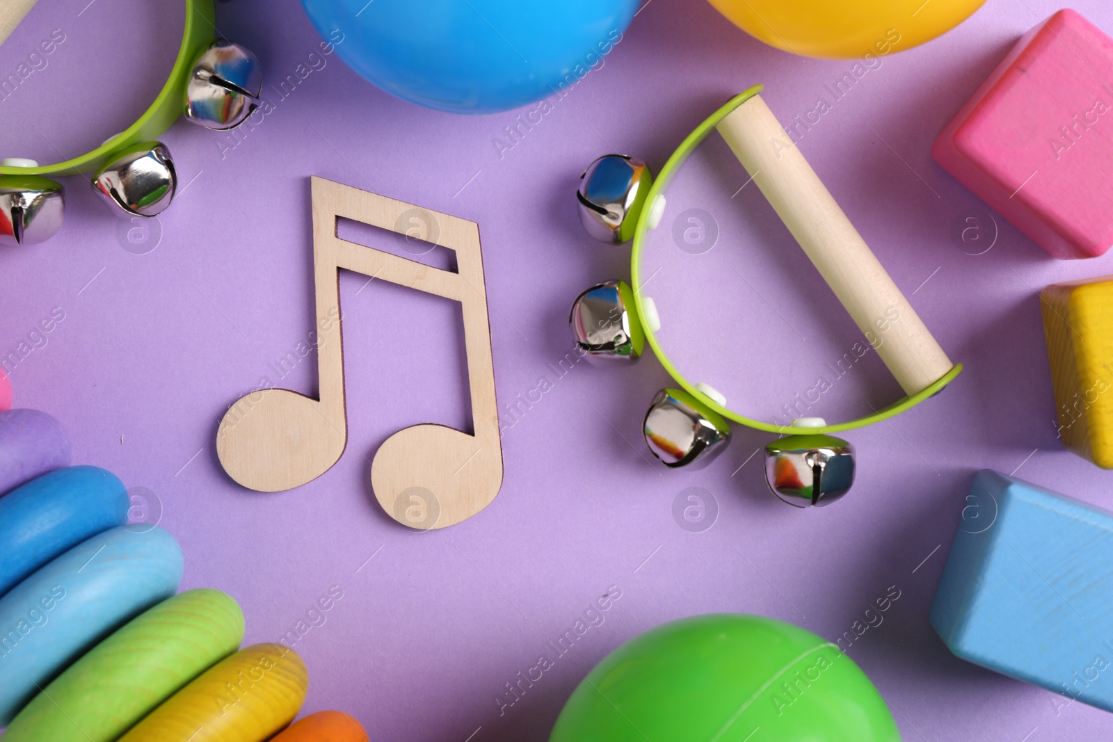 Photo of Tools for creating baby songs. Flat lay composition with wooden note and tambourines for kids on violet background