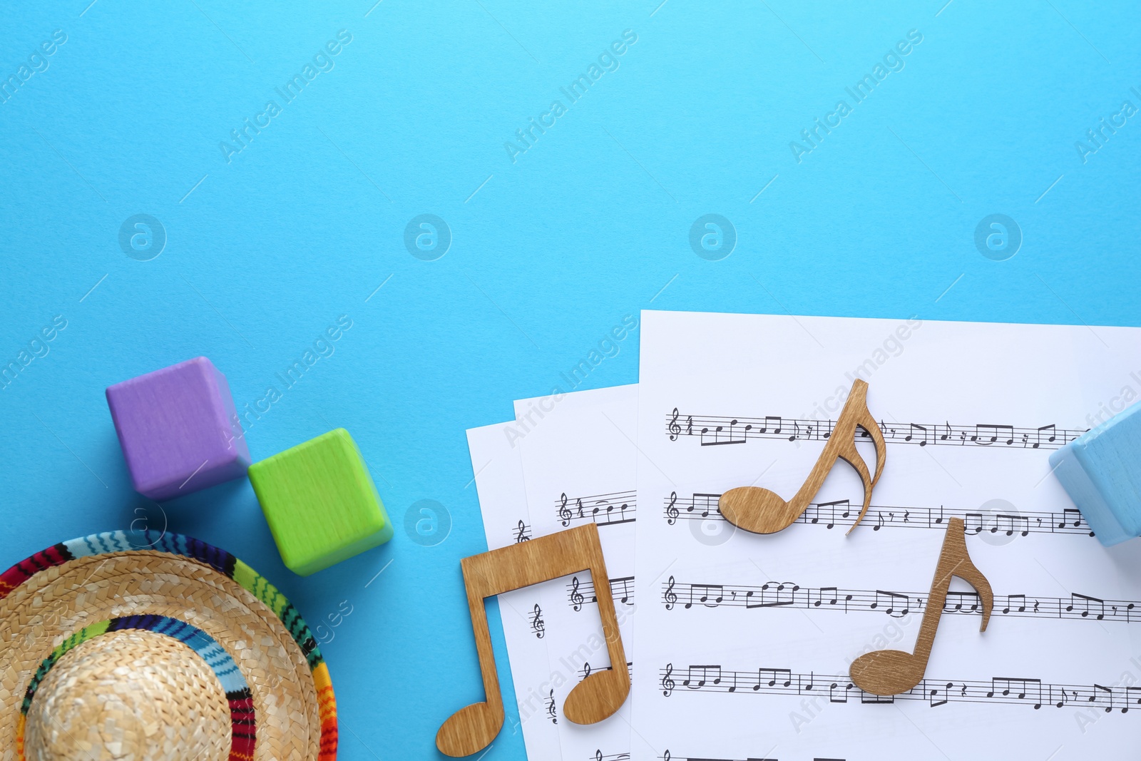 Photo of Baby songs. Music sheets, wooden notes, cubes and hat on light blue background, flat lay with space for text