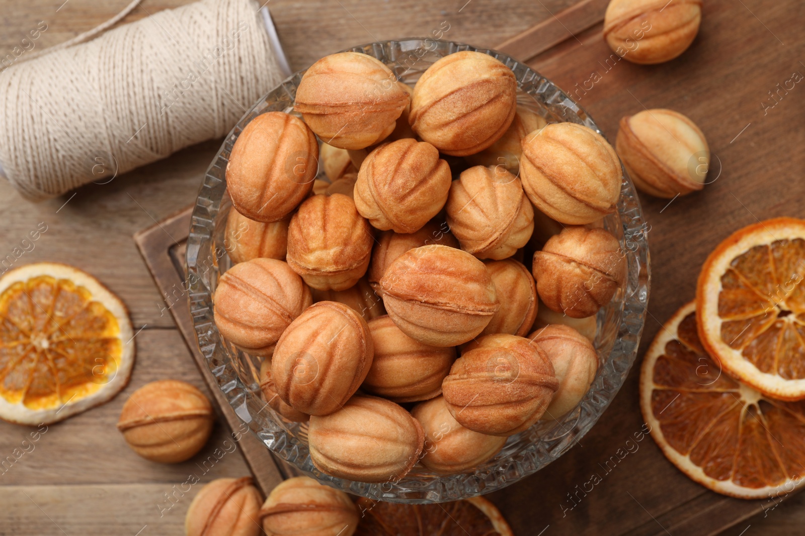 Photo of Bowl of delicious nut shaped cookies and dried orange slices on wooden table, flat lay