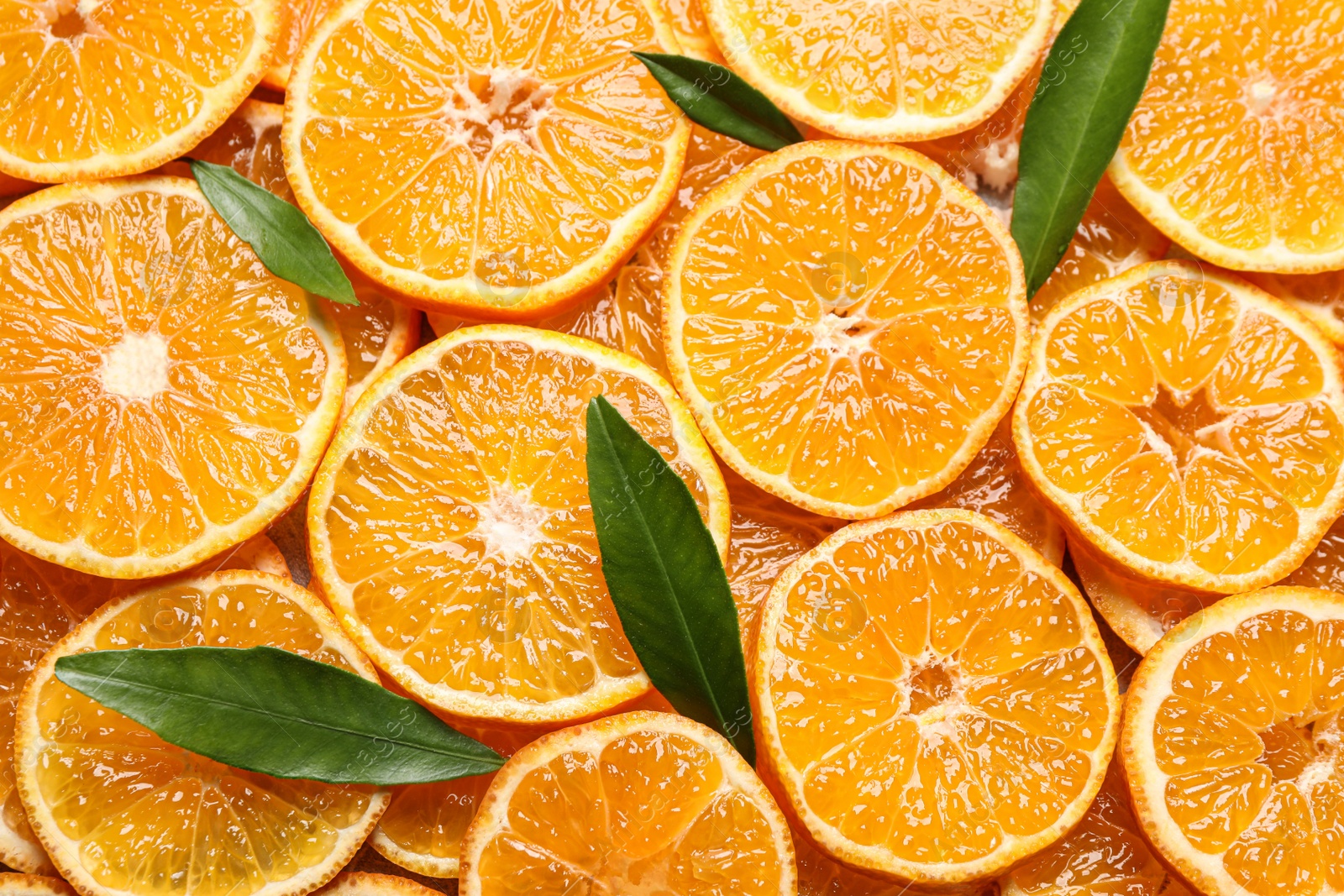 Photo of Slices of fresh ripe tangerines and leaves as background, top view. Citrus fruit