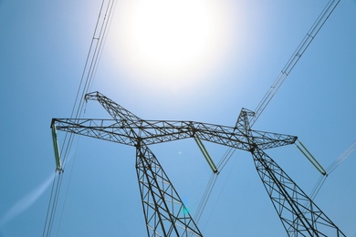 High voltage tower with electricity transmission power lines against blue sky, low angle view