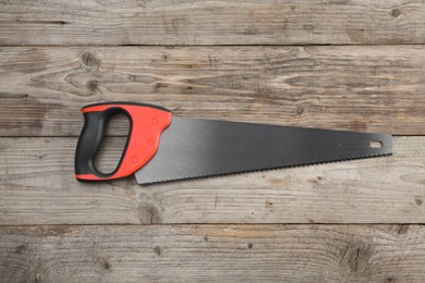 Photo of Saw with colorful handle on wooden background, top view