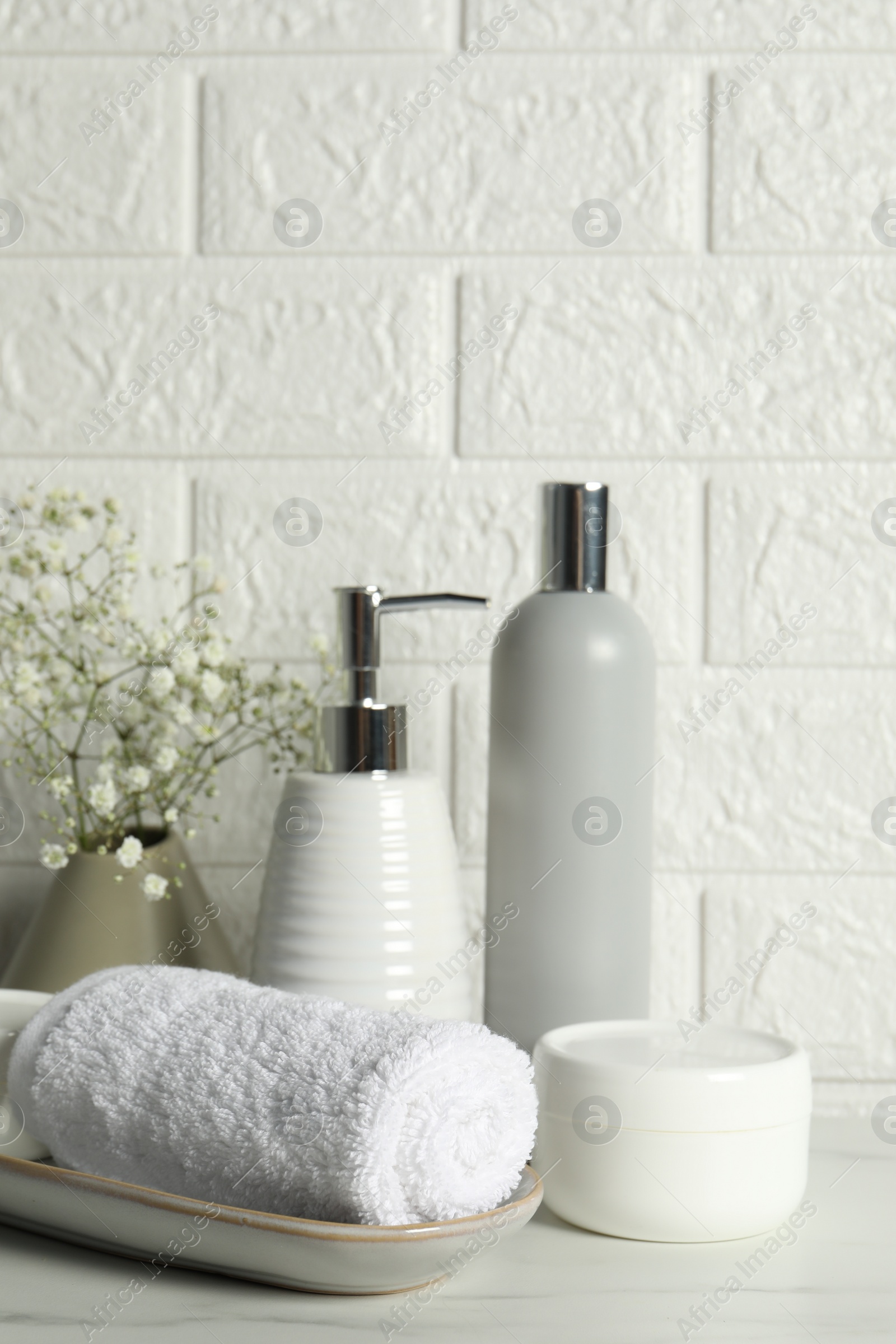 Photo of Different bath accessories, personal care products and gypsophila flowers in vase on white table near brick wall