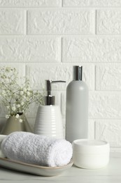 Photo of Different bath accessories, personal care products and gypsophila flowers in vase on white table near brick wall