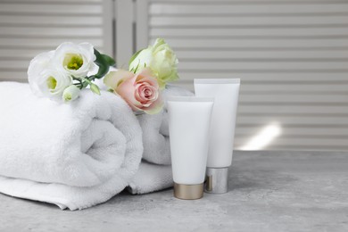 Photo of Towels, cosmetic products and flowers on grey table indoors