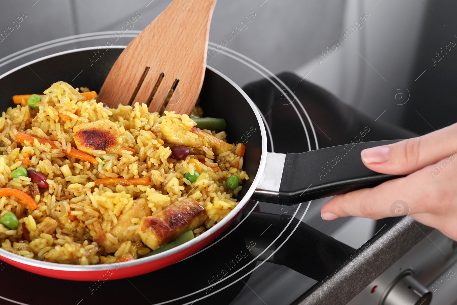 Photo of Woman frying rice with meat and vegetables on induction stove, closeup