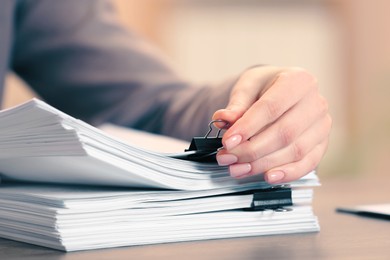 Photo of Woman attaching documents with metal binder clip at table in office, closeup