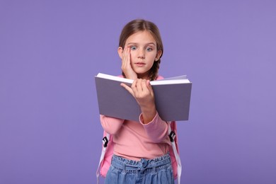 Schoolgirl with open book on violet background