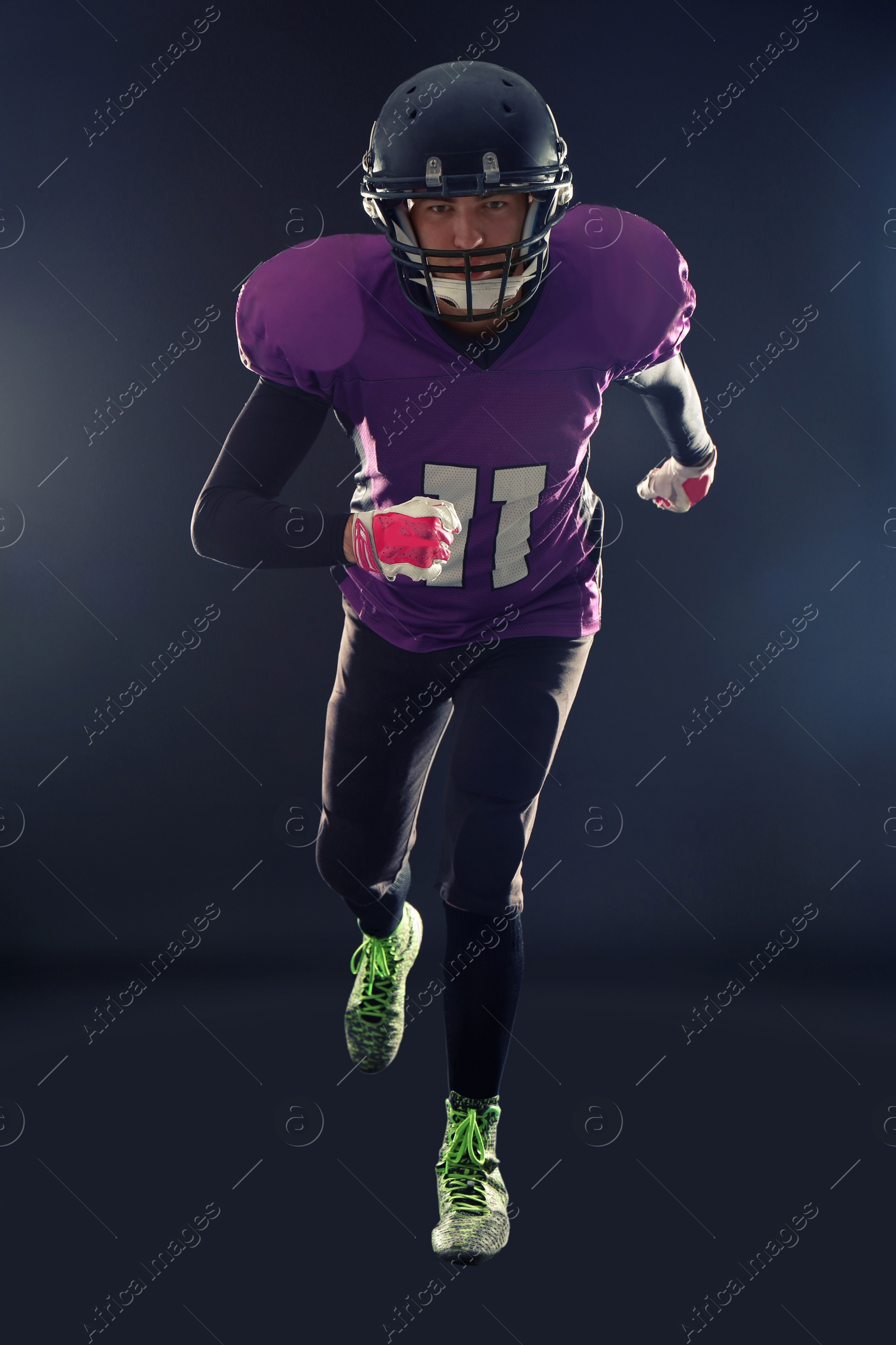 Photo of American football player in uniform running on dark background