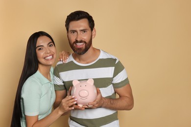 Photo of Happy couple with ceramic piggy bank on beige background