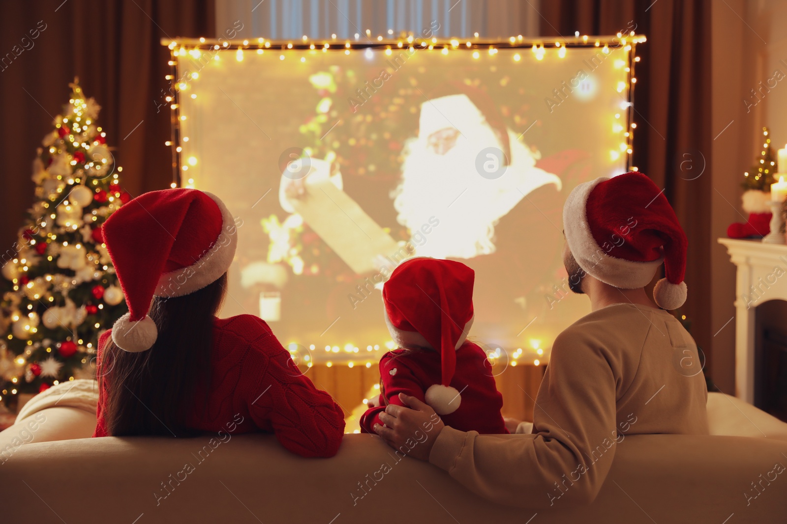 Photo of Family watching movie on projection screen in room decorated for Christmas, back view. Home TV equipment