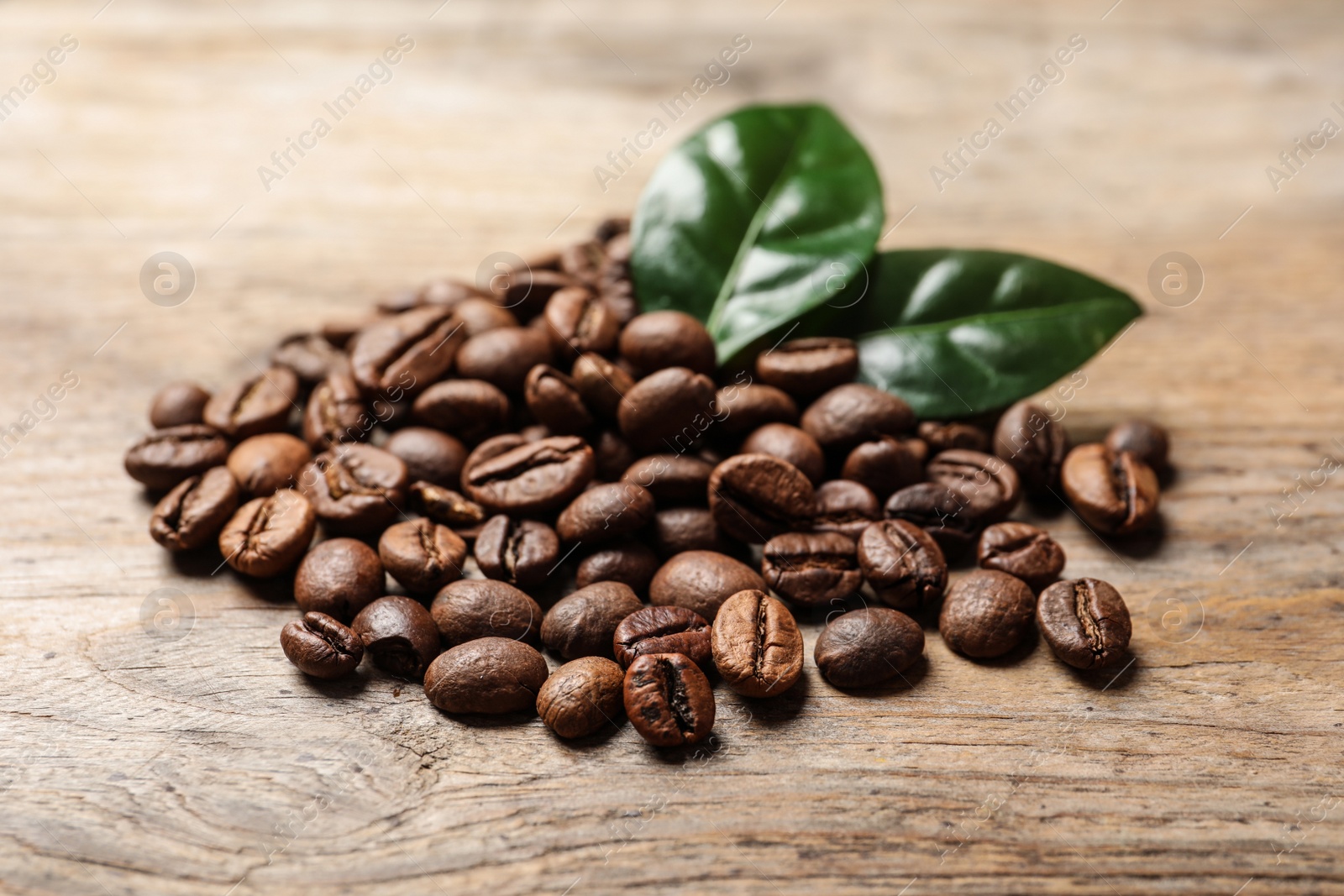 Photo of Pile of coffee beans and fresh green leaves on wooden table
