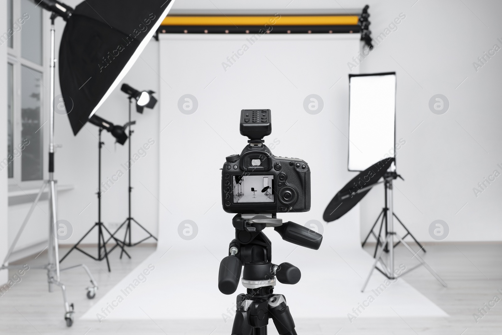 Photo of Camera on tripod, bar stool and professional lighting equipment in modern photo studio