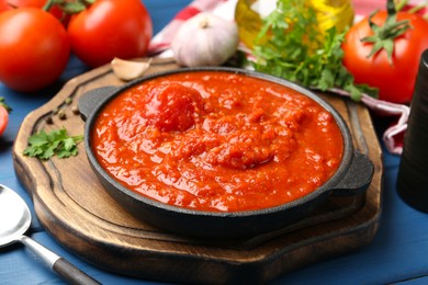 Photo of Homemade tomato sauce in bowl and ingredients on blue table, closeup