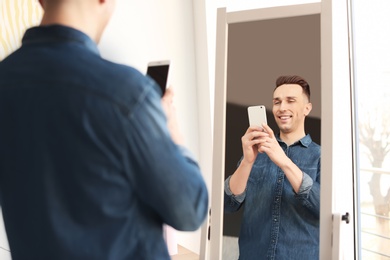 Photo of Young man taking selfie in front of mirror at home