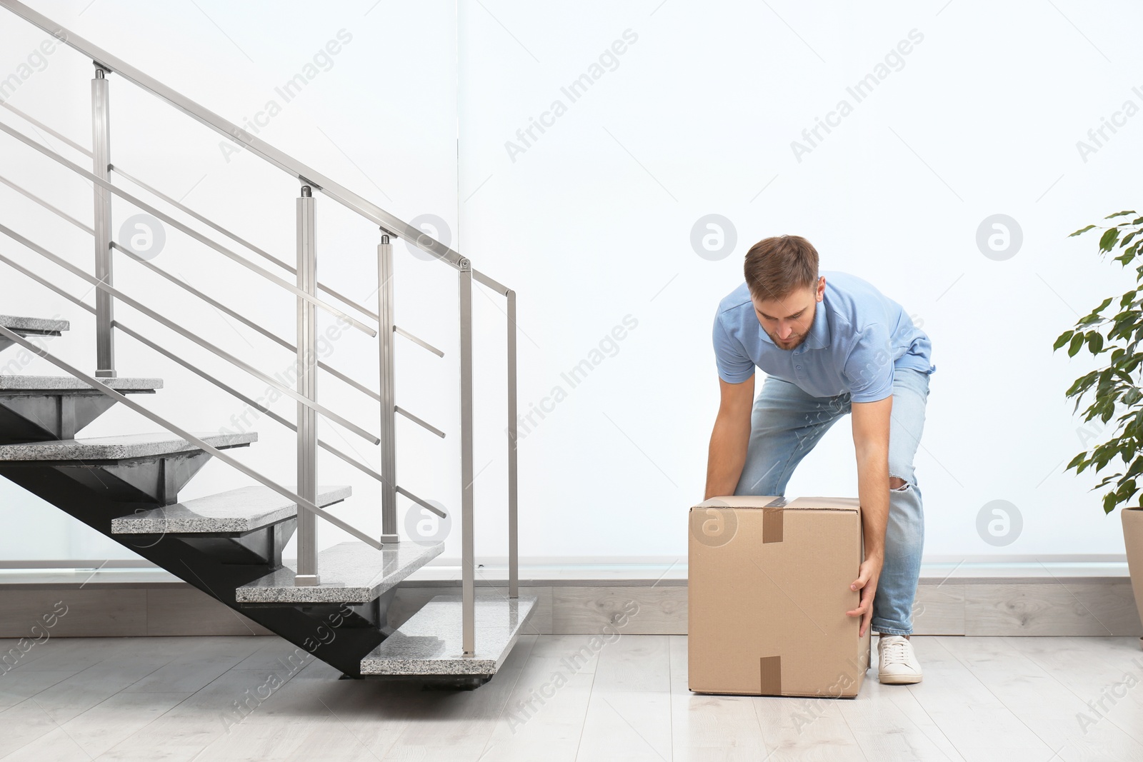 Photo of Young man lifting carton box indoors. Posture concept
