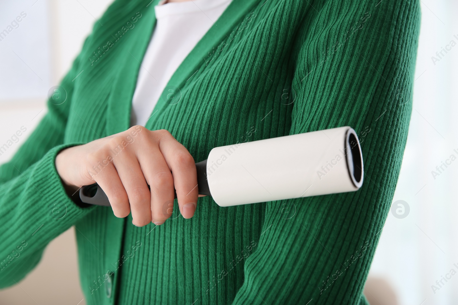 Photo of Woman cleaning green jacket with lint roller on light background, closeup