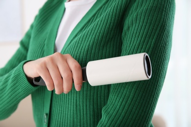 Photo of Woman cleaning green jacket with lint roller on light background, closeup