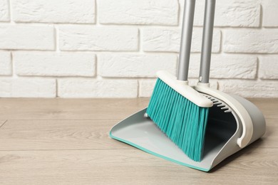 Photo of Plastic broom with dustpan near white brick wall indoors. Space for text