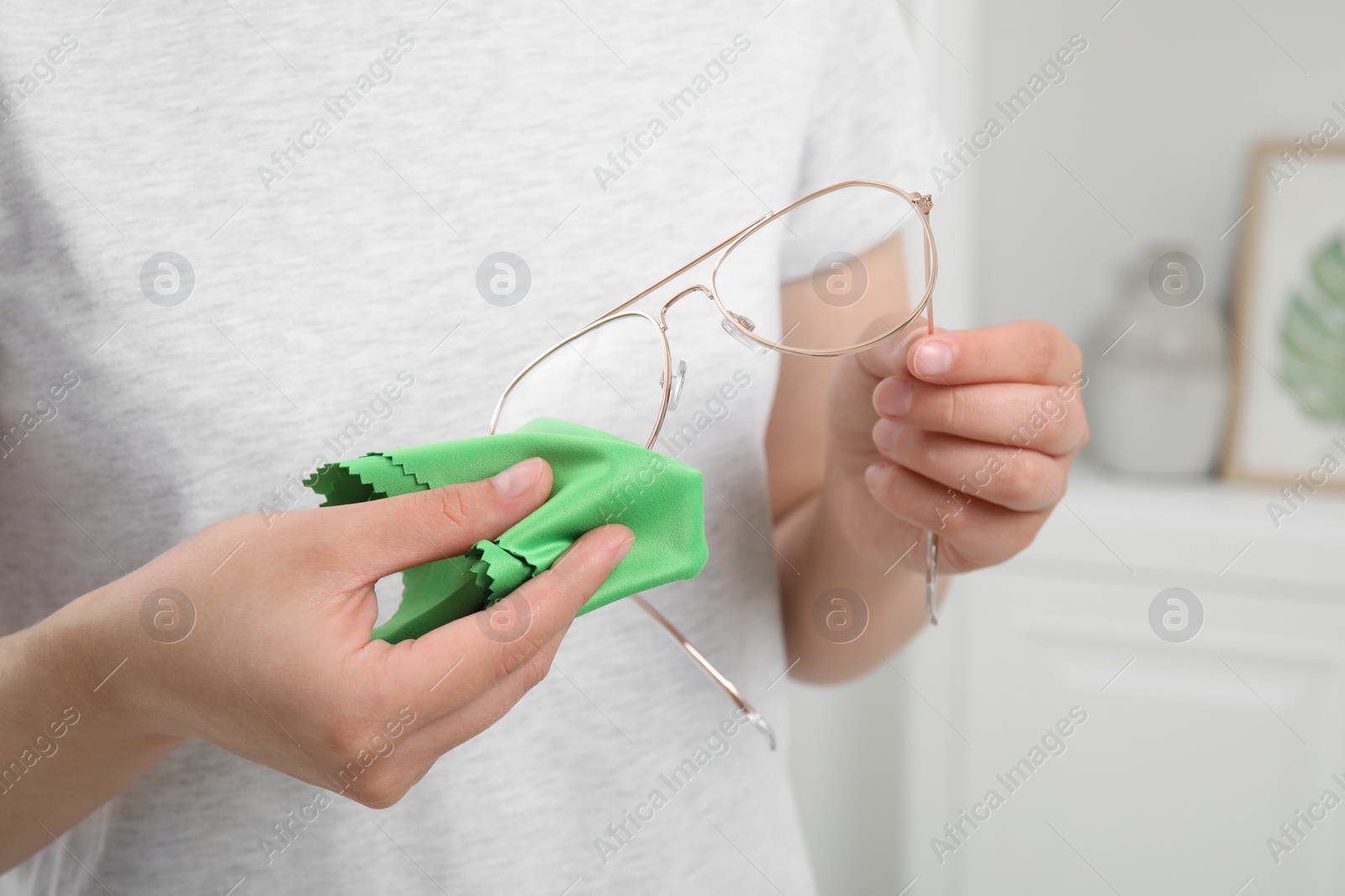 Photo of Woman wiping her glasses with microfiber cloth at home, closeup