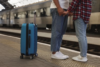 Photo of Long-distance relationship. Couple holding hands on platform of railway station, closeup
