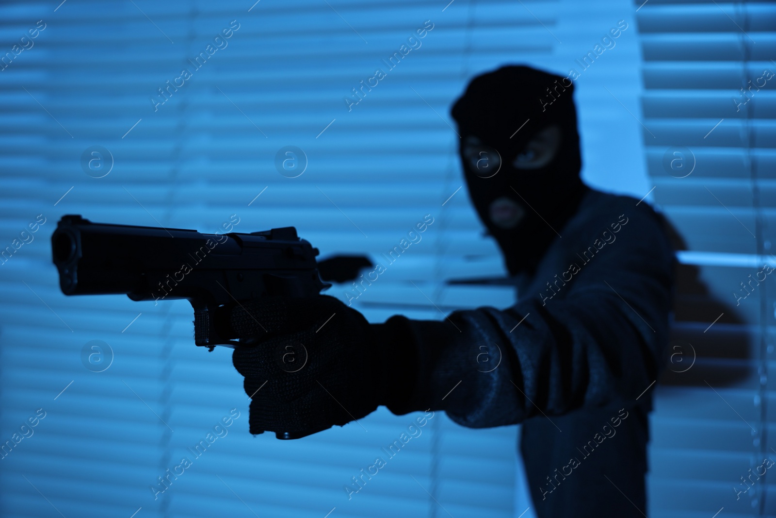 Photo of Thief with gun coming out of blinds at night, selective focus. Burglary