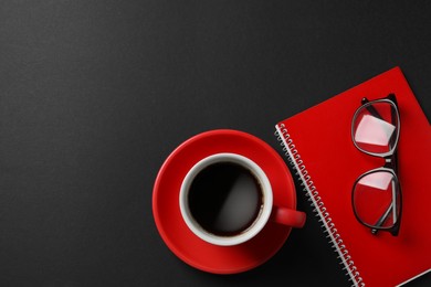 Photo of Cup with aromatic coffee, notepad and glasses on black background, flat lay. Space for text