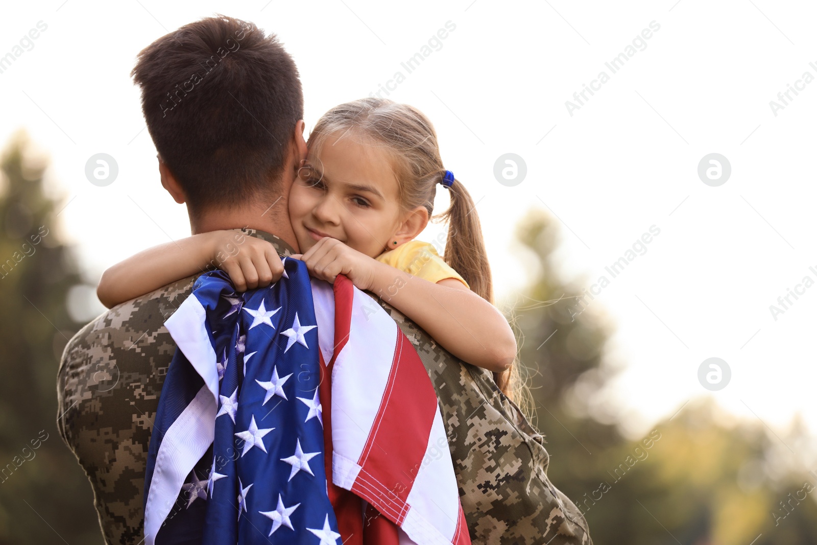 Photo of Father in military uniform with American flag and his daughter at sunny park