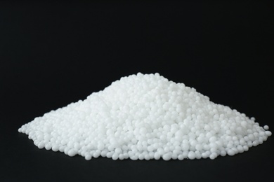 Photo of Pellets of ammonium nitrate on black background, space for text. Mineral fertilizer