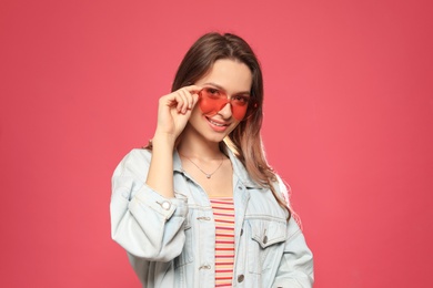 Portrait of beautiful young woman with heart shaped sunglasses on color background