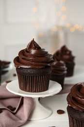 Dessert stand with delicious chocolate cupcake on white table against blurred lights