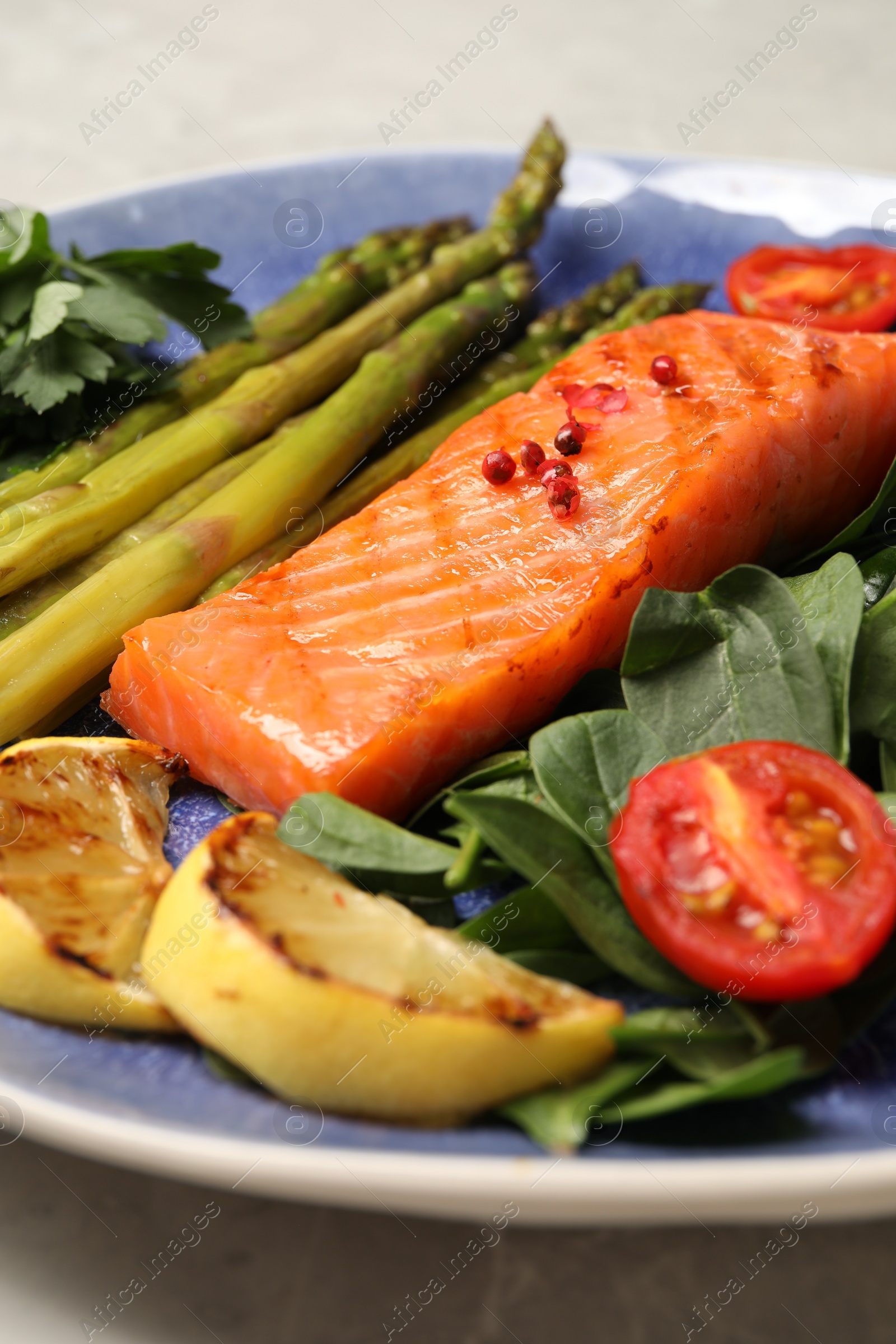 Photo of Tasty grilled salmon with tomatoes, asparagus, lemon and basil on grey table, closeup