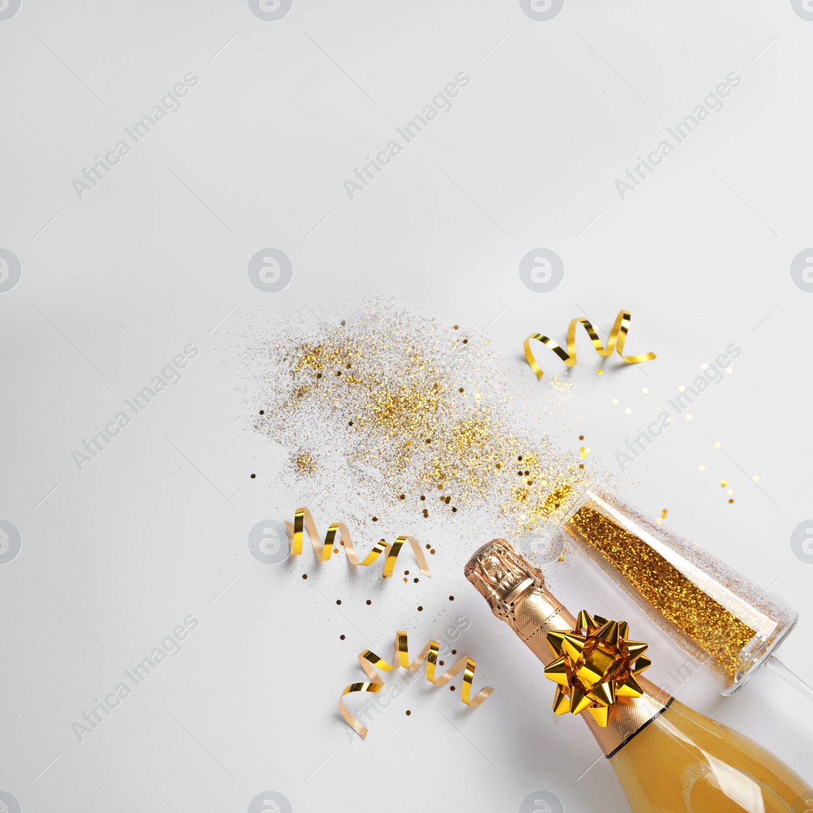 Photo of Bottle of champagne, glass with gold glitter and space for text on white background, top view. Hilarious celebration