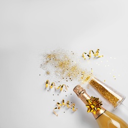 Bottle of champagne, glass with gold glitter and space for text on white background, top view. Hilarious celebration