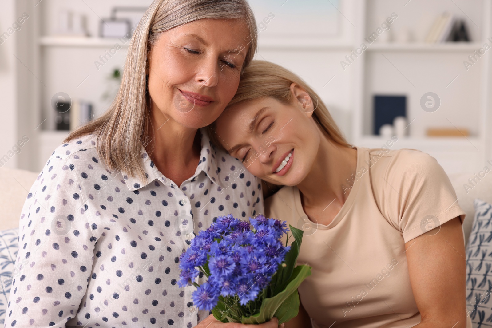 Photo of Happy mature mother and her daughter with beautiful cornflowers at home