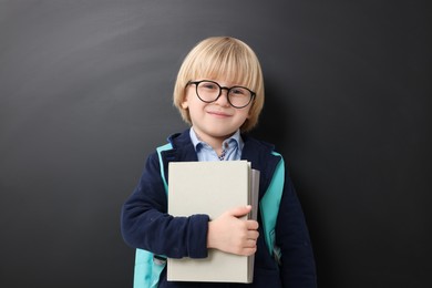 Photo of Happy little school child with notebooks near chalkboard