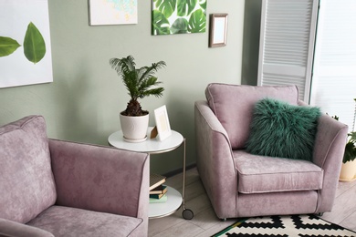 Photo of Tropical plant with green leaves and comfortable armchairs in room interior