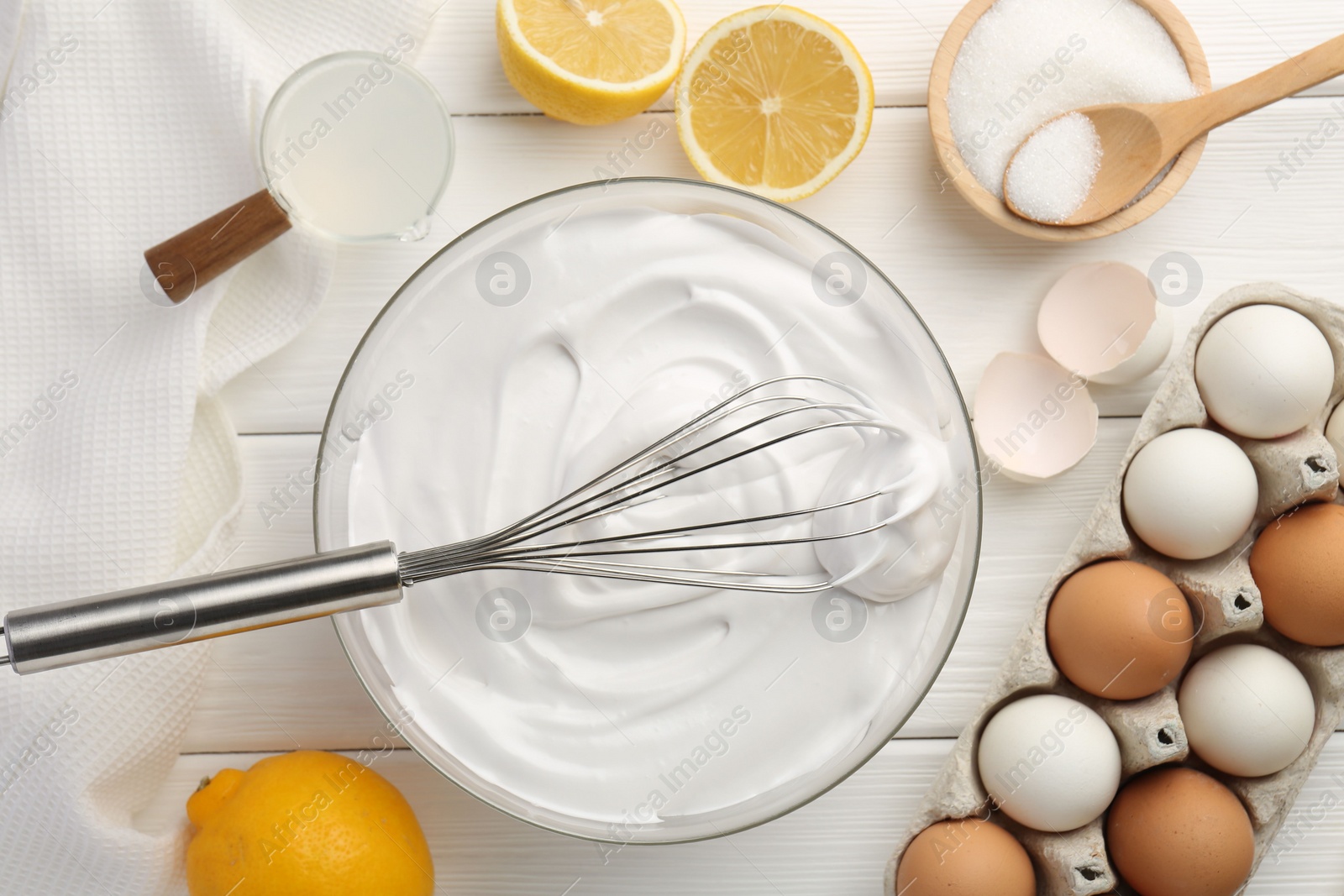 Photo of Bowl with whipped cream, whisk and ingredients on white wooden table, flat lay