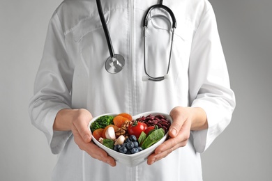 Photo of Doctor holding bowl with products for heart-healthy diet on color background, closeup